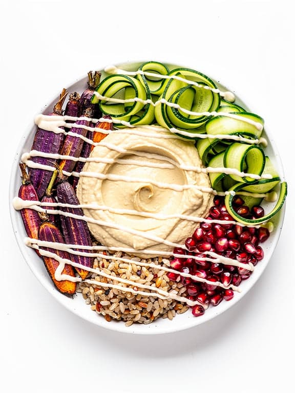 Vibrant Mediterranean grain bowl. Large scoop of Zaaki hummus as the centerpiece. Surrounded by roasted purple carrots, bright green cucumber ribbons, and fresh pomegranate pearls. Drizzled with white tahini. High-saturation colors, clean white background. Healthy lifestyle aesthetic. High resolution